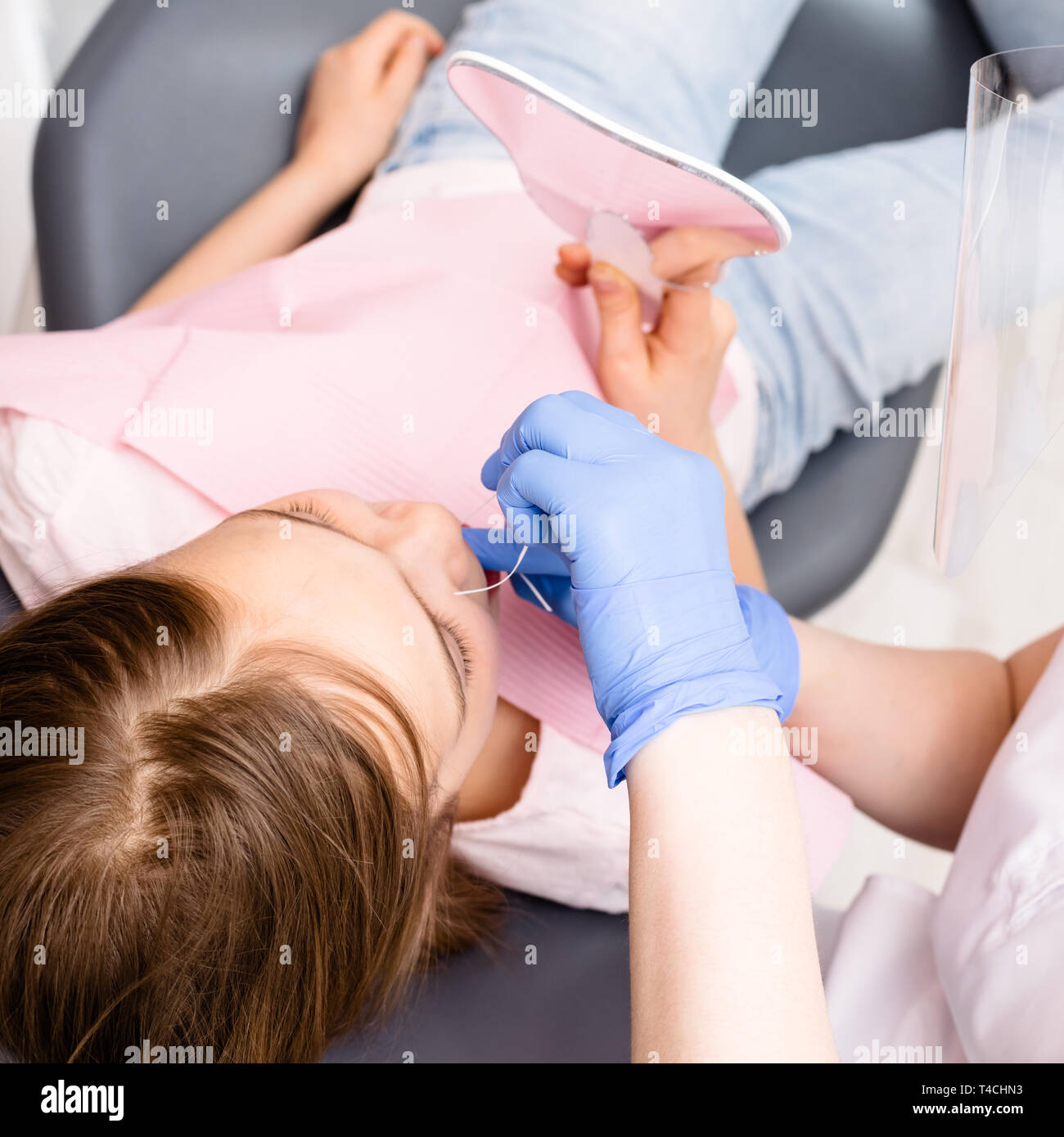 Dentista pediatrico che mostra elementari di età ragazza come usare il filo interdentale per rimuovere la placca tra i denti nella clinica dentale. Bambino seduto in un dentista di c Foto Stock