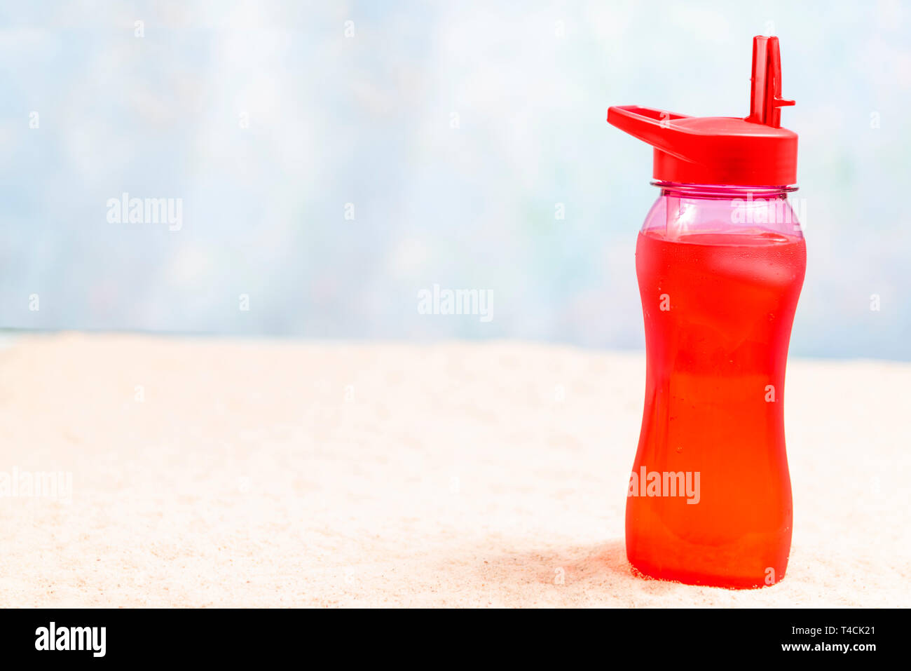 Inquadratura orizzontale di un fuori fuoco sfondo sulla spiaggia con una bevanda di colore rosso per un puntello. Bere è sul lato destro. Copia dello spazio. Foto Stock