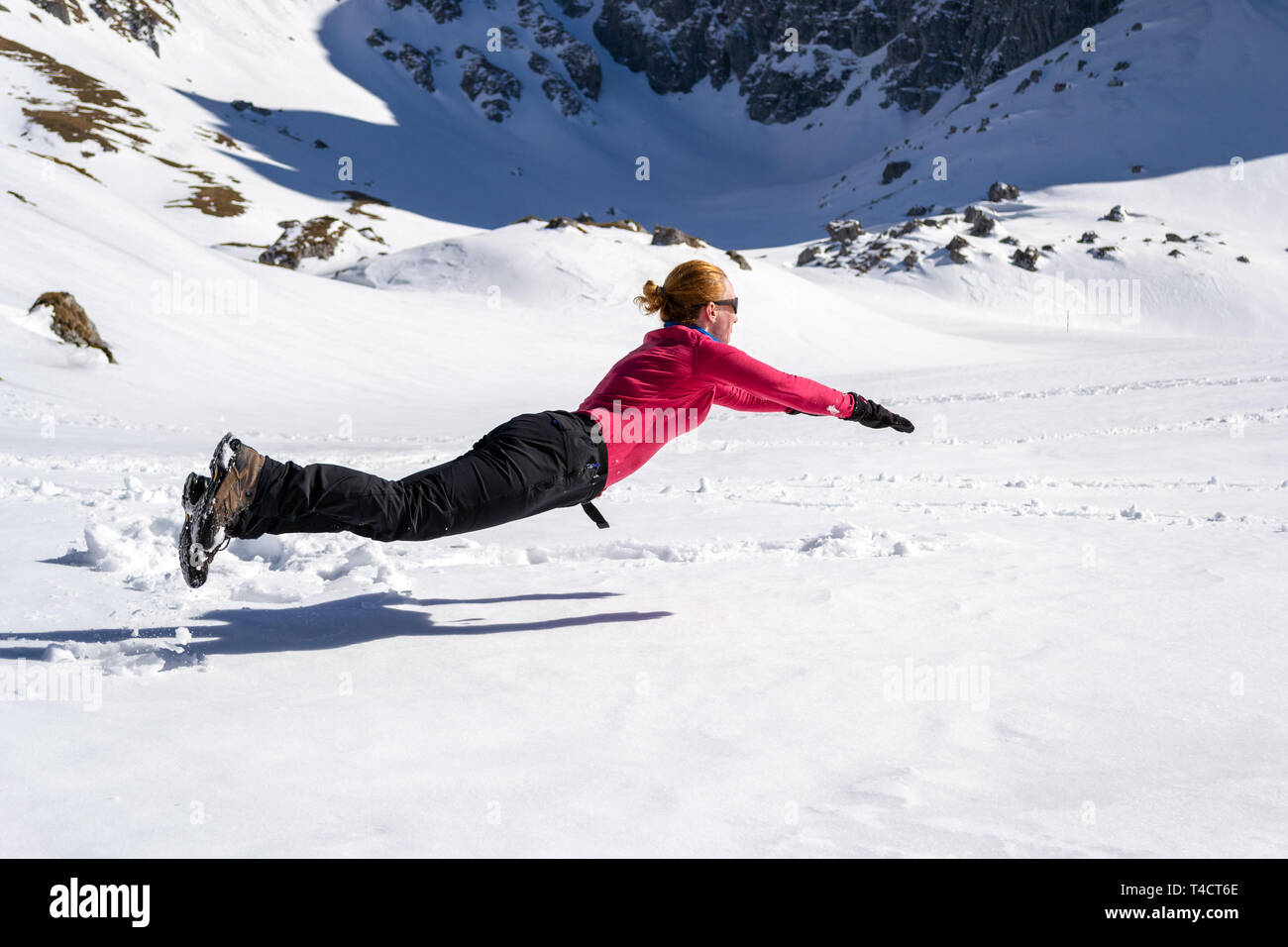 Femmina gioiosa escursionista saltellando sulla neve, orizzontalmente, somigliante ad un Superman/Superwoman pongono la levitazione, vicino Malaiesti hut, Bucegi/moun dei Carpazi Foto Stock