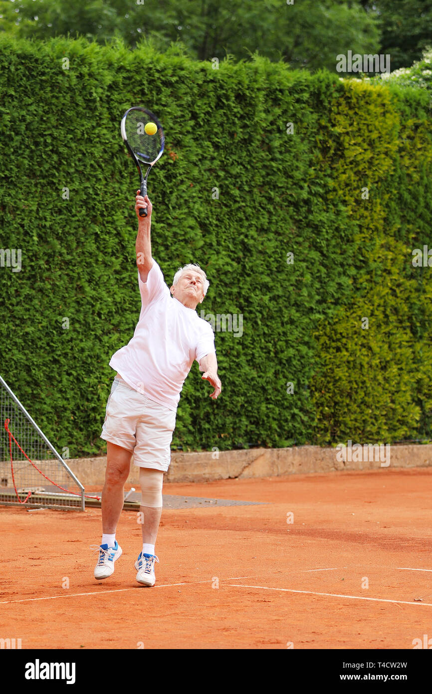 Il vecchio uomo attivo che serve la sfera sul match di tennis Foto Stock