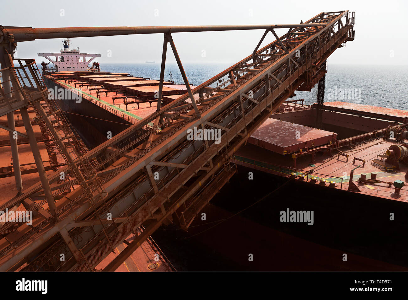 Operazioni portuali per la gestione e il trasporto di minerale di ferro. Lo scarico di minerale di ammende dal TGV transhipper barca in attesa di OGV ocean andando peschereccio in mare Foto Stock