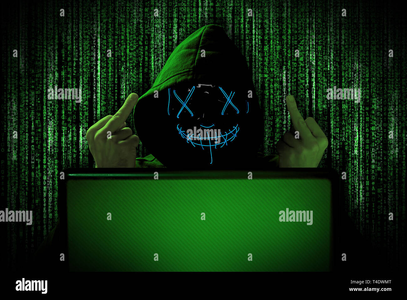 Hacker con dita mediane gesto provocazione blu brillante maschera dietro notebook portatile di fronte fonte verde codice binario sfondo cyber internet Foto Stock