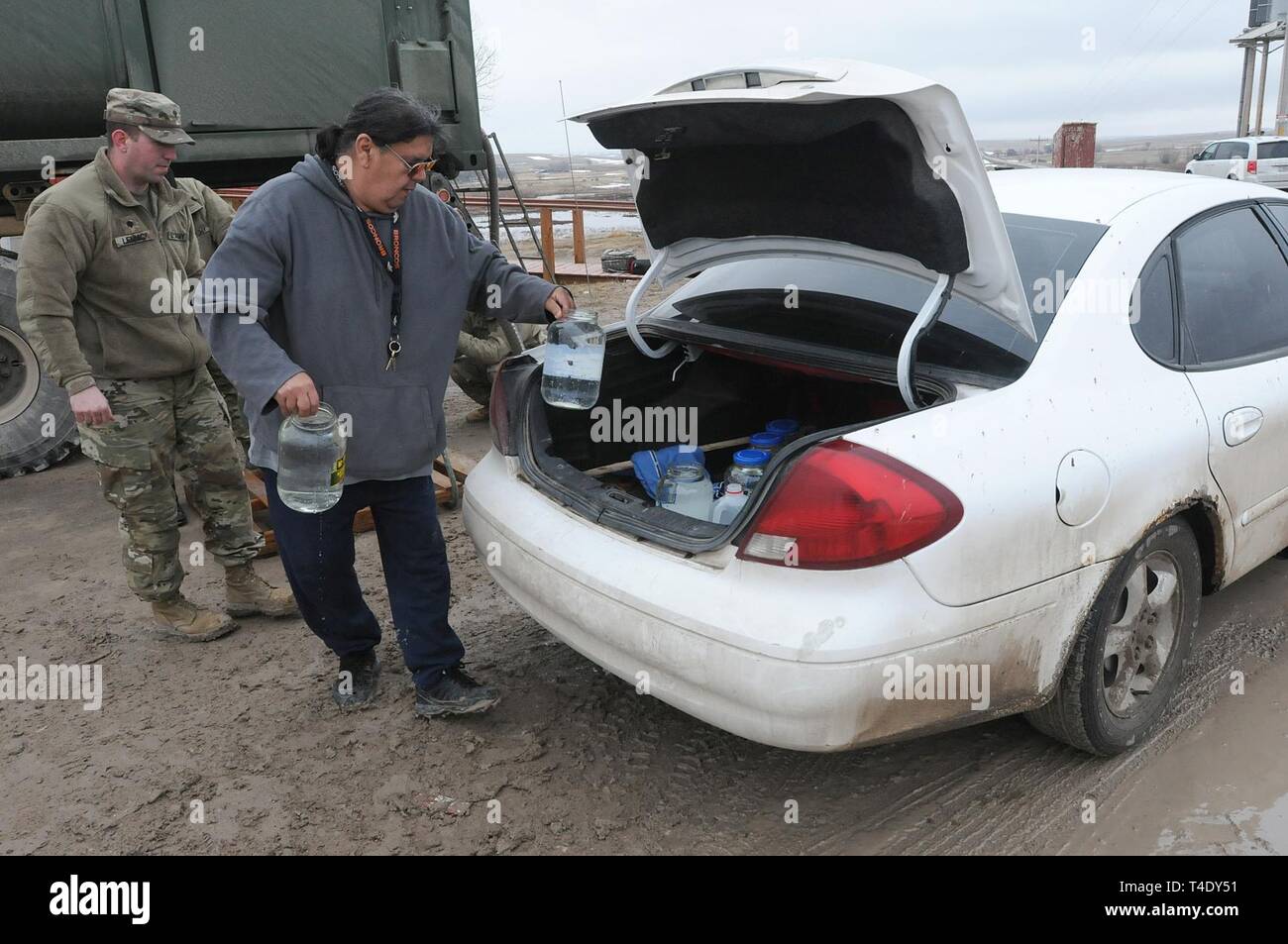 Lester Rowland carichi di contenitori di acqua potabile nella sua automobile con l aiuto degli Stati Uniti Army Spc. Tracy Lennick, società A, 139a supporto dei vigili del Battaglione, South Dakota Esercito nazionale di protezione, a stacciature angolo su Pine Ridge Reservation, Marzo 25, 2019. Tredici SDARNG soldati sono stati attivati per dovere di stato in Pine Ridge dopo una contea galleggiamento non riuscita a causa di inondazioni estreme lasciando i residenti in sette europee senza acqua nelle loro case. Foto Stock