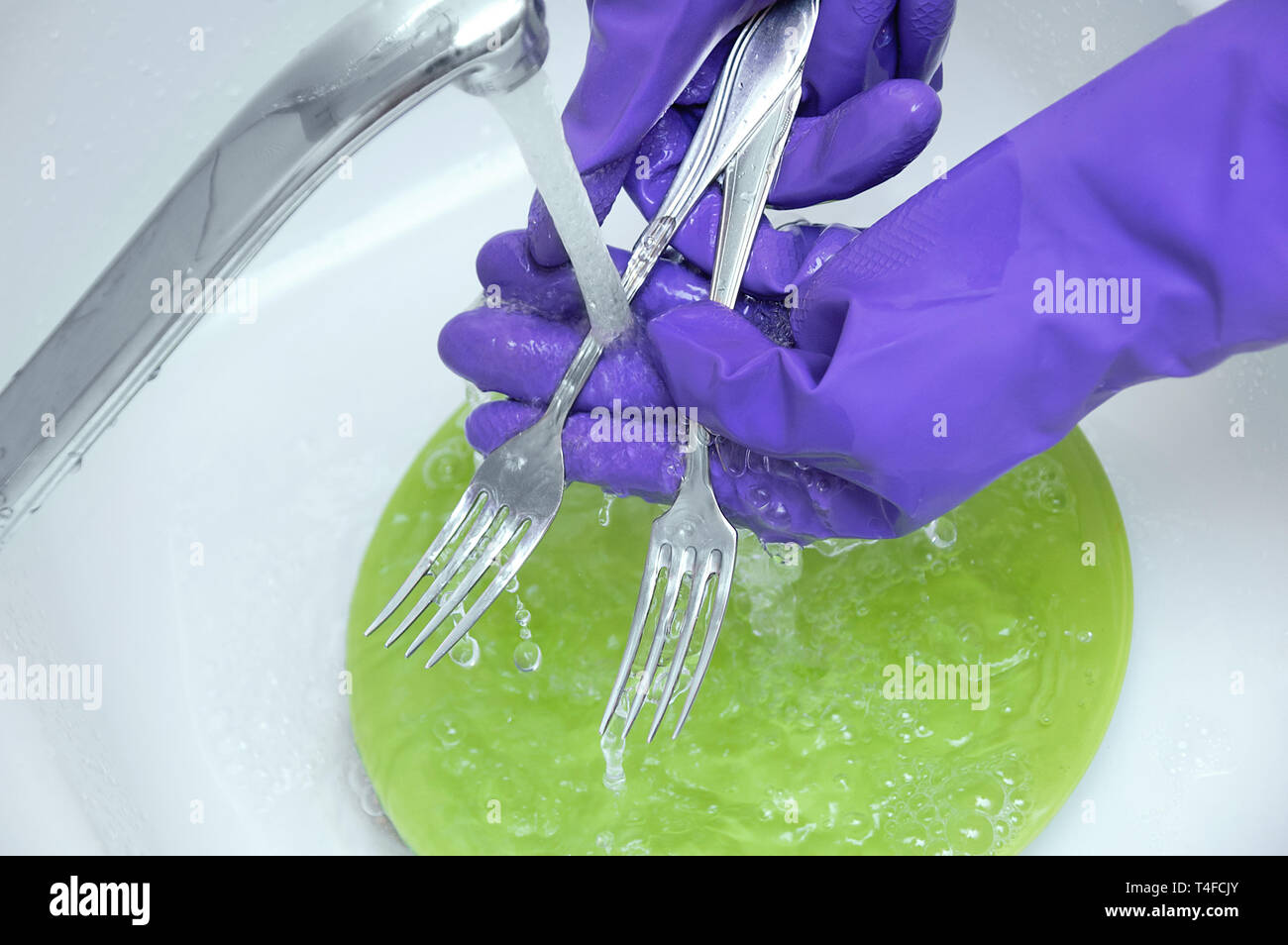 Piatti di lavaggio sotto acqua corrente. Mani in guanti protettivi in gomma. Foto Stock