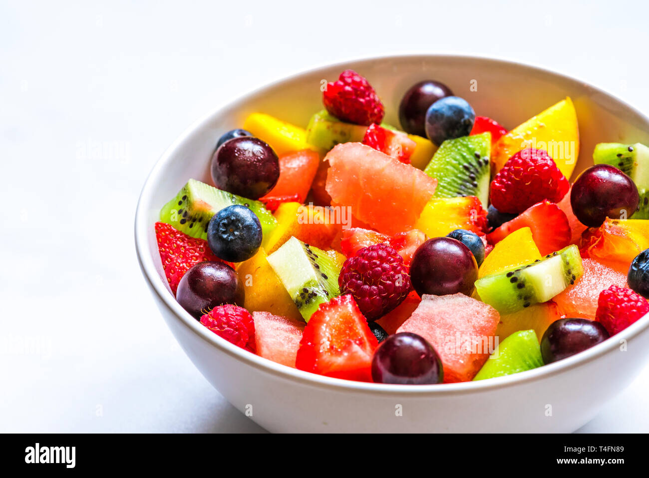 Ciotola di frutta estiva e insalata di Berry su marmo bianco dello sfondo. sano cibo vegan. close up Foto Stock