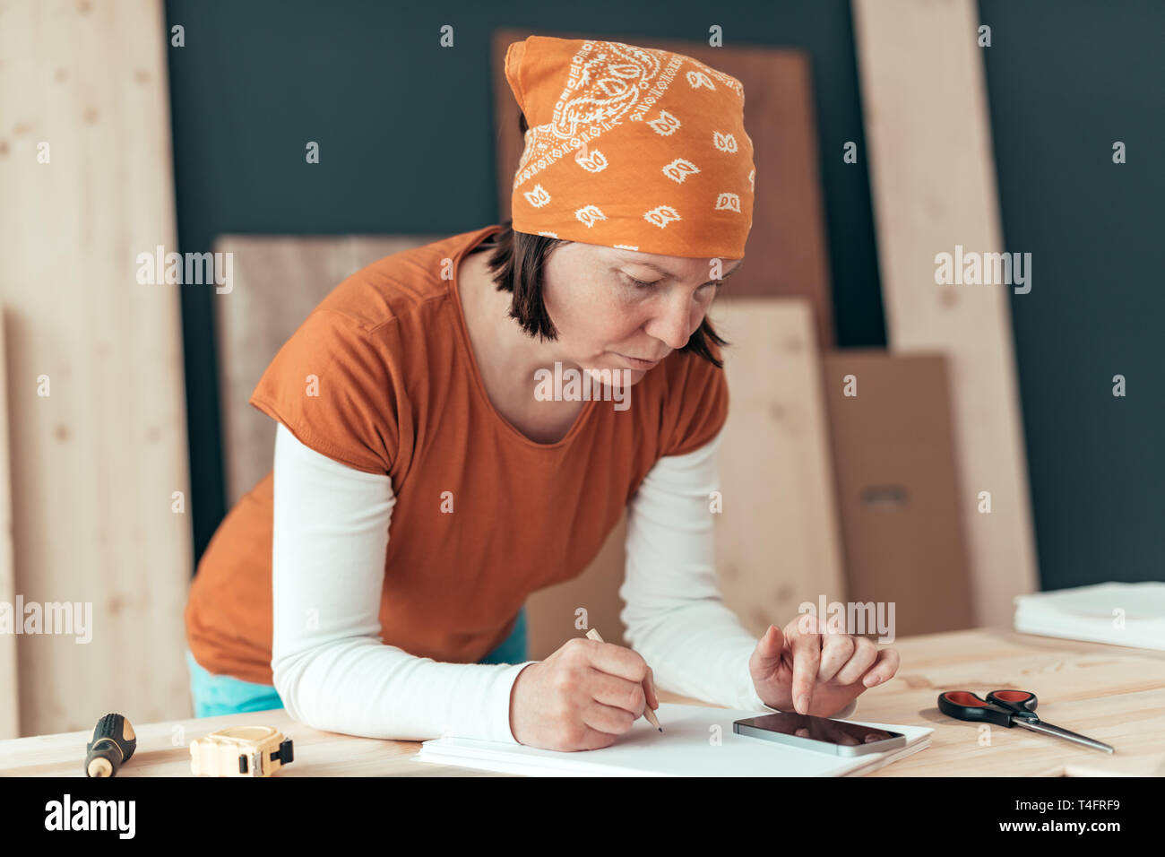 Falegname femmina con il fazzoletto di testa facendo il calcolo finanziario in falegnameria officina di falegnameria Foto Stock
