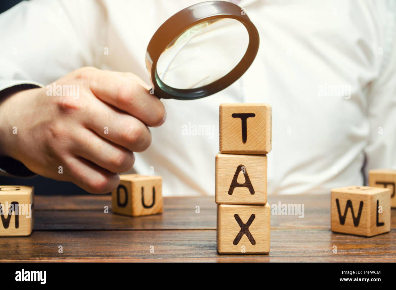 Blocchi di legno con la parola fiscale e di una lente di ingrandimento nelle mani di un imprenditore. Il concetto di studiare la dimensione delle imposte. Imposizione fiscale. Il termine di pagamento Foto Stock