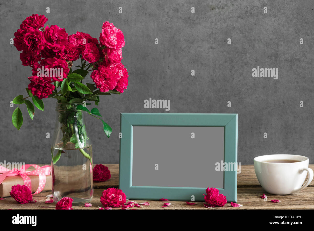 Blank photo frame e rose fiori con tazza di tè e confezione regalo su tavola in legno rustico. mock up. matrimonio o womens giorno concetto. still life Foto Stock