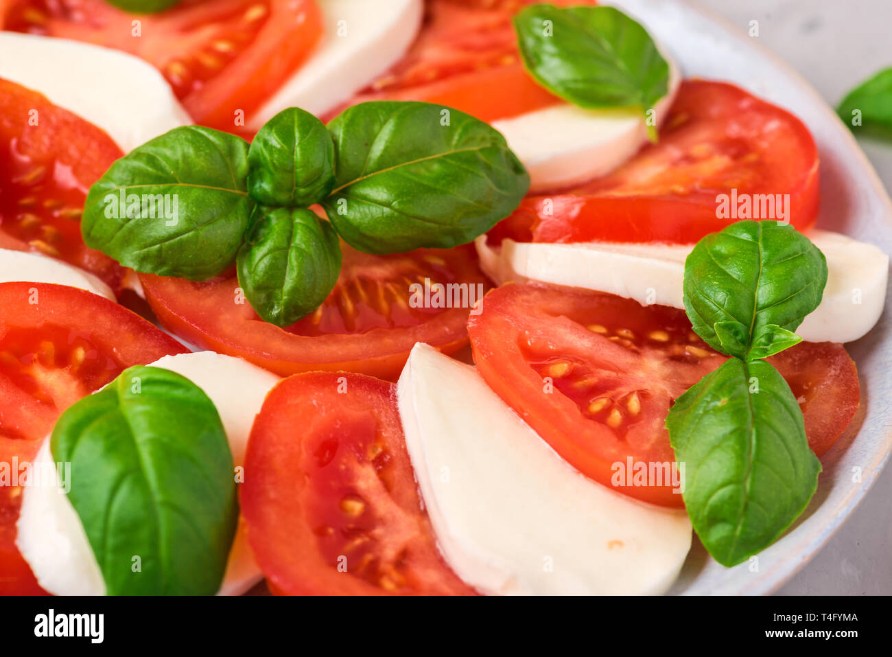 Italiano insalata caprese con pomodori a fette, formaggio mozzarella, basilico, olio d'oliva in una piastra sul cemento grigio Sfondo. close up Foto Stock