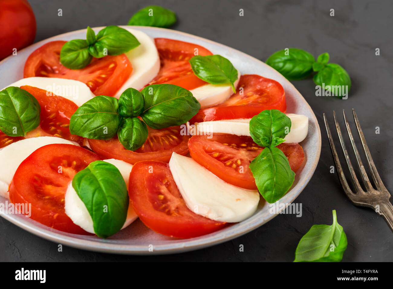 Insalata caprese con pomodori maturi e mozzarella, di foglie di basilico fresco su calcestruzzo scuro dello sfondo. Il cibo italiano. close up Foto Stock