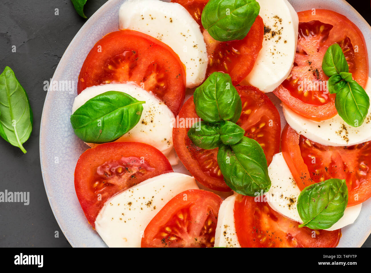 Close up italiano insalata caprese con pomodori a fette, formaggio mozzarella, basilico, olio d'oliva, pepe in una piastra sul calcestruzzo scuro dello sfondo. laici piana. Foto Stock