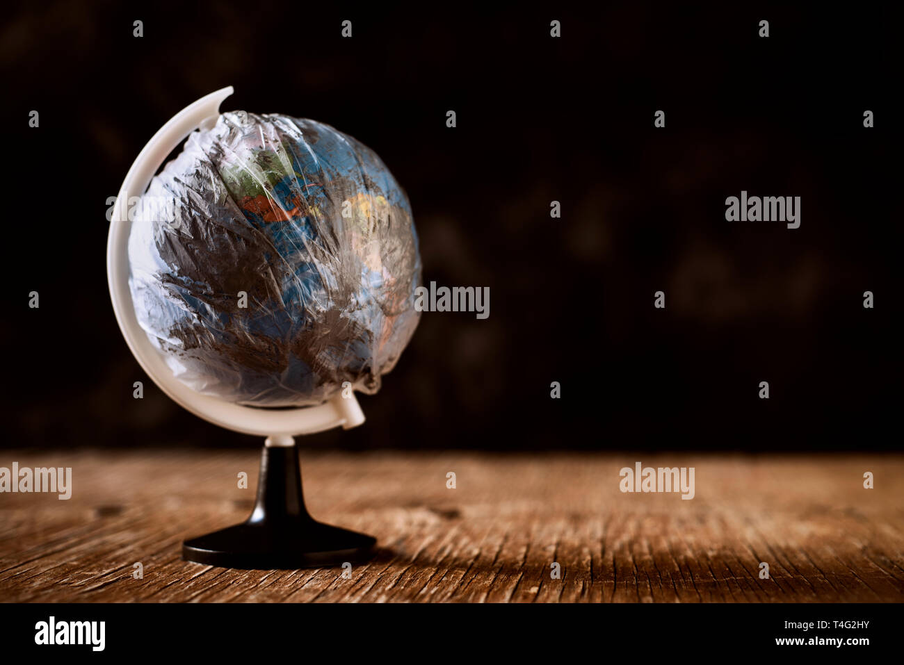 Un globo mondo avvolto in una plastica sporca, su un rustico di una superficie di legno, contro uno sfondo scuro, raffigurante l'inquinamento atmosferico, l'eccesso di materiale plastico wa Foto Stock