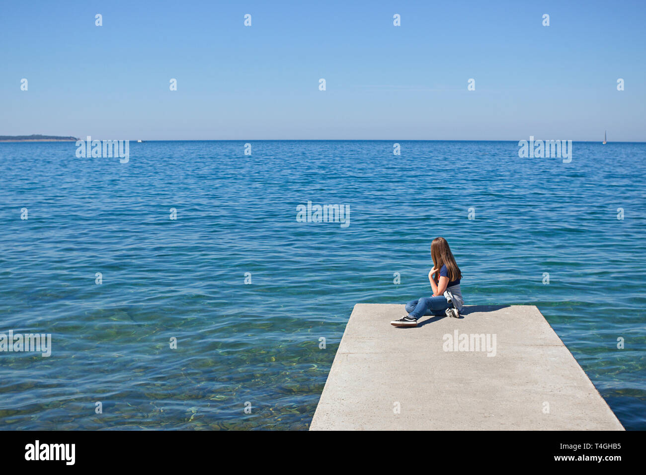 Ragazza adolescente solo sul molo da un mare turchese Foto Stock