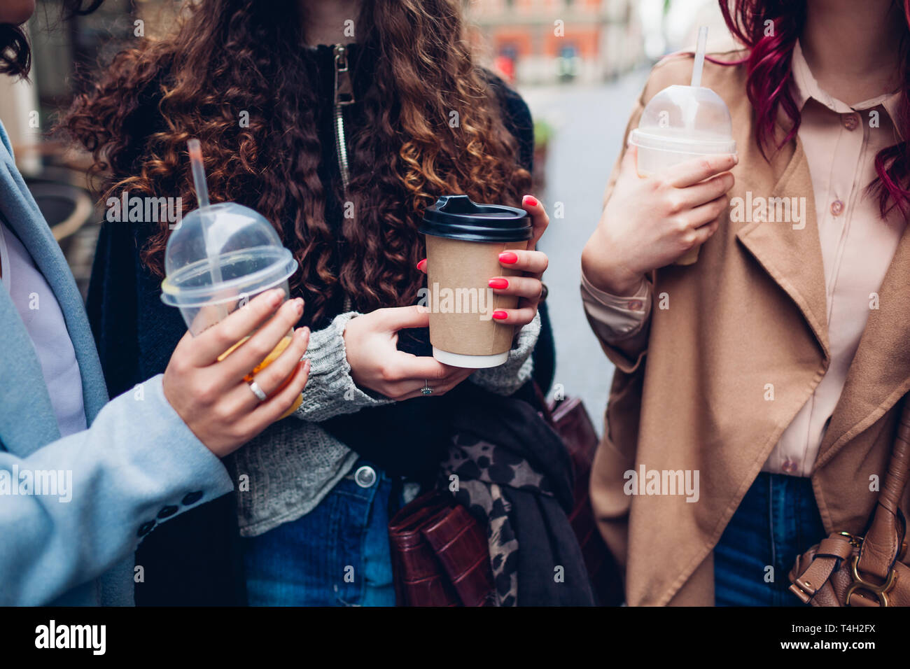 Tre amici di sesso femminile avente un drink all'aperto. Felici donne tintinnio caffè, succo d'arancia e tazze di tè Foto Stock