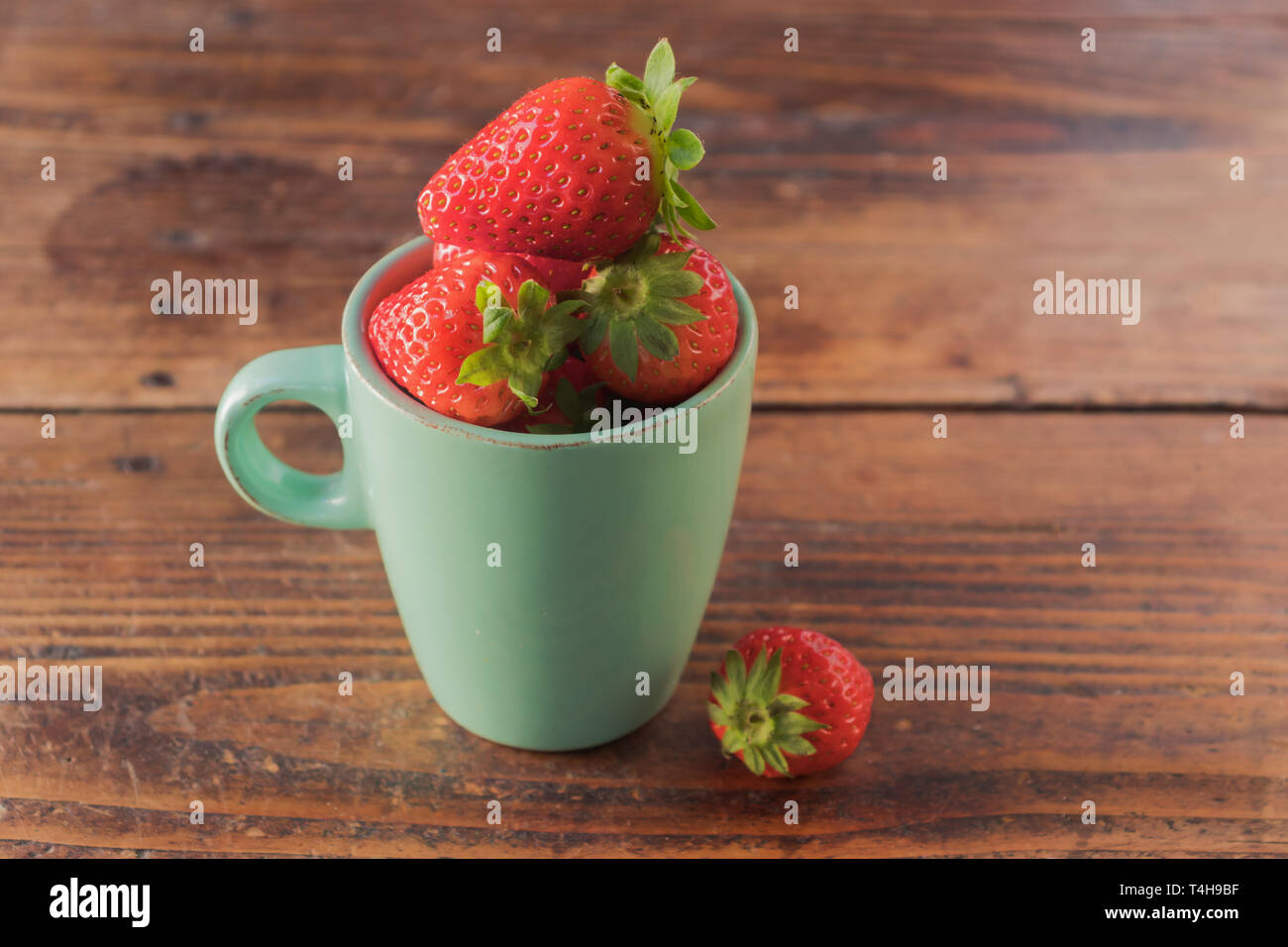 Acquamarina tazza di porcellana pieno di fragole rosso, su un sfondo di legno Foto Stock