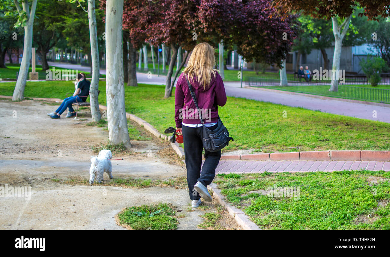 Donna bionda prende il suo cane per una passeggiata con un guinzaglio in un percorso al parco. Le donne a piedi cane a parchi in Murcia, Spagna, 2019 Foto Stock