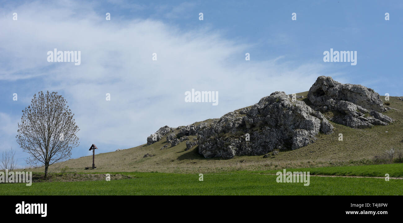 16 aprile 2019, il Land della Baviera, Nördlingen: in corrispondenza del bordo del cratere Ries vi è una croce accanto a una formazione rocciosa. Il Nördlinger Ries, formata da un meteorite impatto, roccia ha delle strutture simili a quelle che si trovano sulla luna. Pertanto la NASA ha inviato la sua astroauts a nord di Svevia per preparare la luna missioni di carico. Foto: Stefan Puchner/dpa Foto Stock