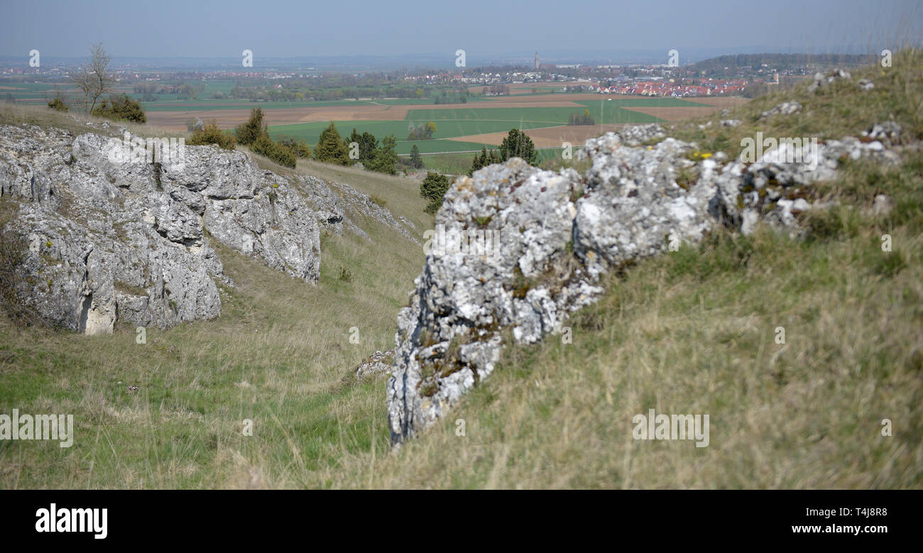 16 aprile 2019, il Land della Baviera, Nördlingen: Dietro aspre rocce si trova la piana del cratere Ries con Daniel chiesa torre della città di Nördlingen. Il Nördlinger Ries, formata da un meteorite impatto, roccia ha delle strutture simili a quelle che si trovano sulla luna. Pertanto la NASA ha inviato la sua astroauts a nord di Svevia per preparare la luna missioni di carico. Foto: Stefan Puchner/dpa Foto Stock