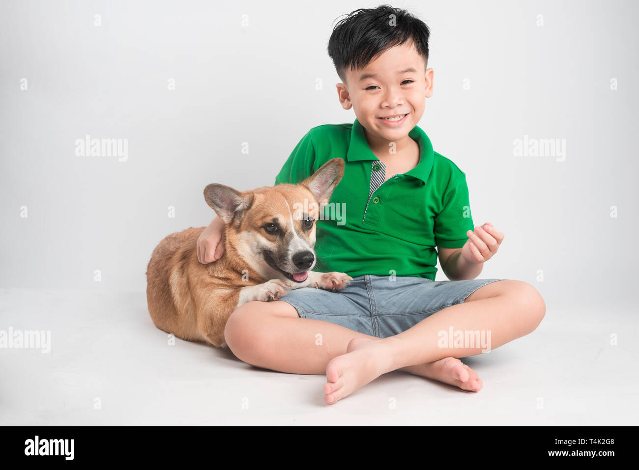 Ritratto di un gioioso little boy divertendosi con welsh corgi cane sul pavimento in studio. Foto Stock