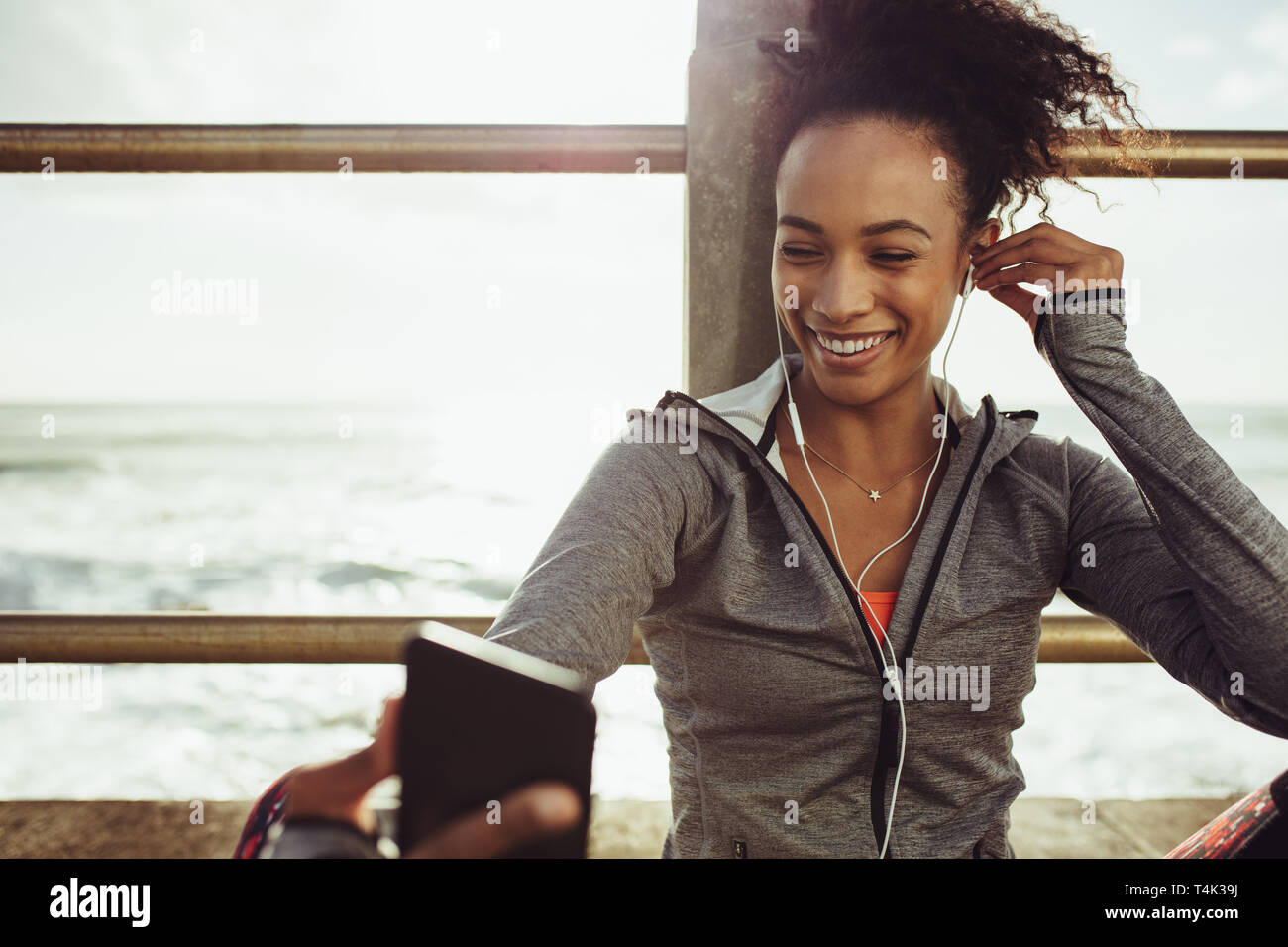 Atleta donna seduta al lungomare e ascoltando la musica dal suo telefono. Runner in appoggio e ascolto di musica durante il corso di formazione di pausa. Foto Stock