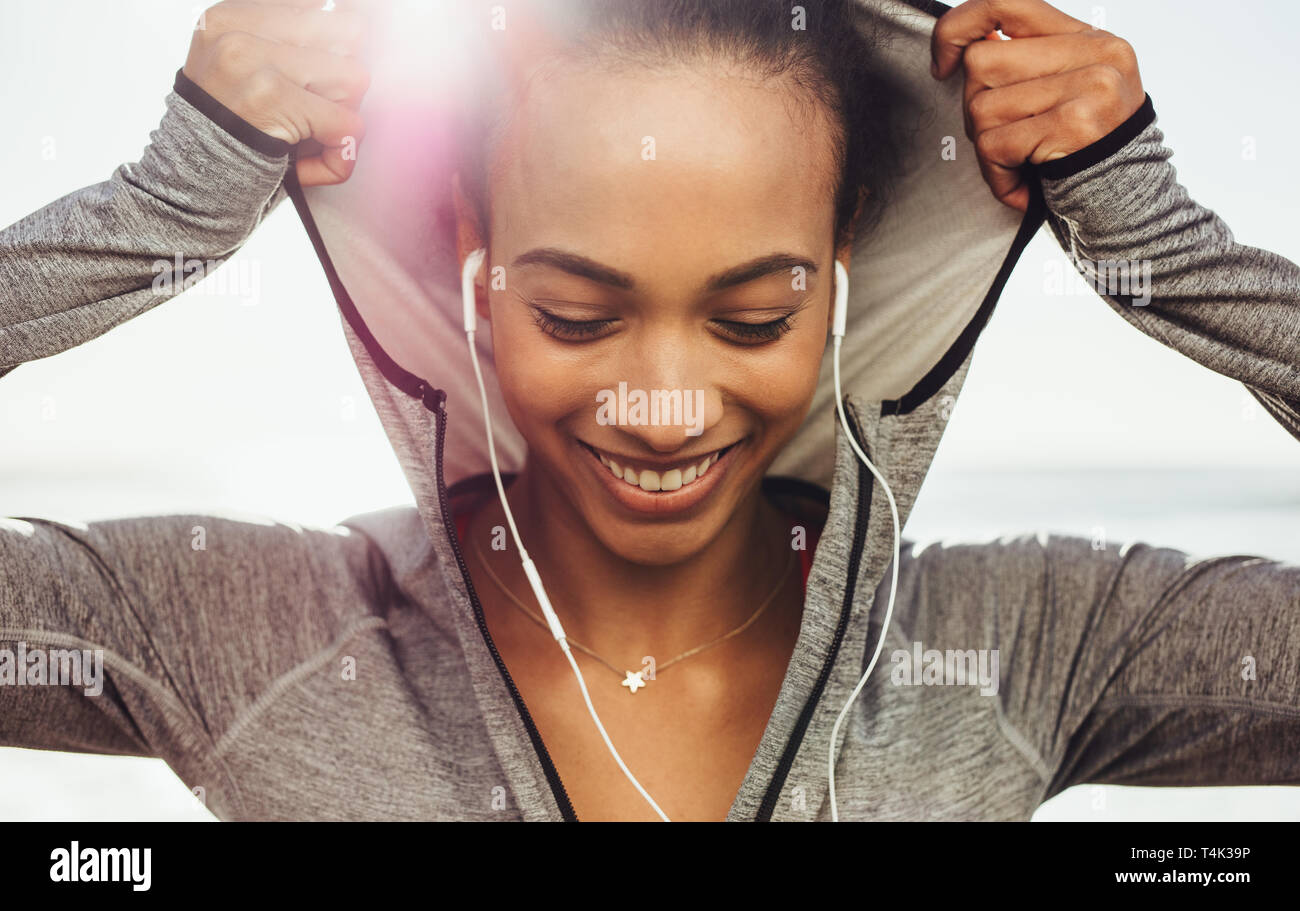 Ravvicinata di una giovane donna che indossa una felpa con cappuccio e sorridente all'esterno. Femminile prendendo una pausa dopo allenamento. Foto Stock