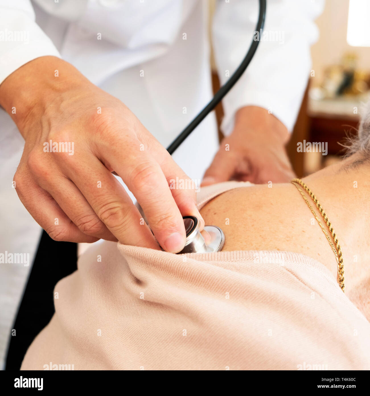 Primo piano di un medico caucasica uomo in camice bianco, auscultating senior caucasica donna paziente utilizzando uno stetoscopio, a casa sua o ad una assistenza infermieristica hom Foto Stock