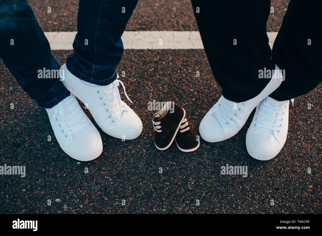 Ritagliato maschio e femmina gambe indossando sneakers bianco tra loro sono sneakers per il loro bambino Foto Stock