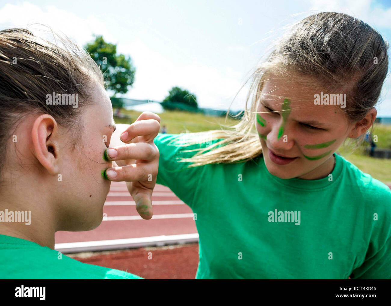 Ragazza putting green face vernice su amico per casa giorno atletica, UK. Foto Stock