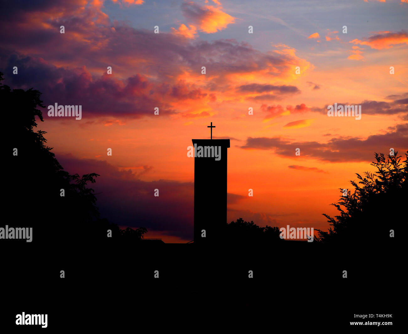 Silhouette della chiesa con la croce con uno spettacolare tramonto e cielo arancione in background. Foto scattata a Bindermichl a Linz, Austria. Foto Stock