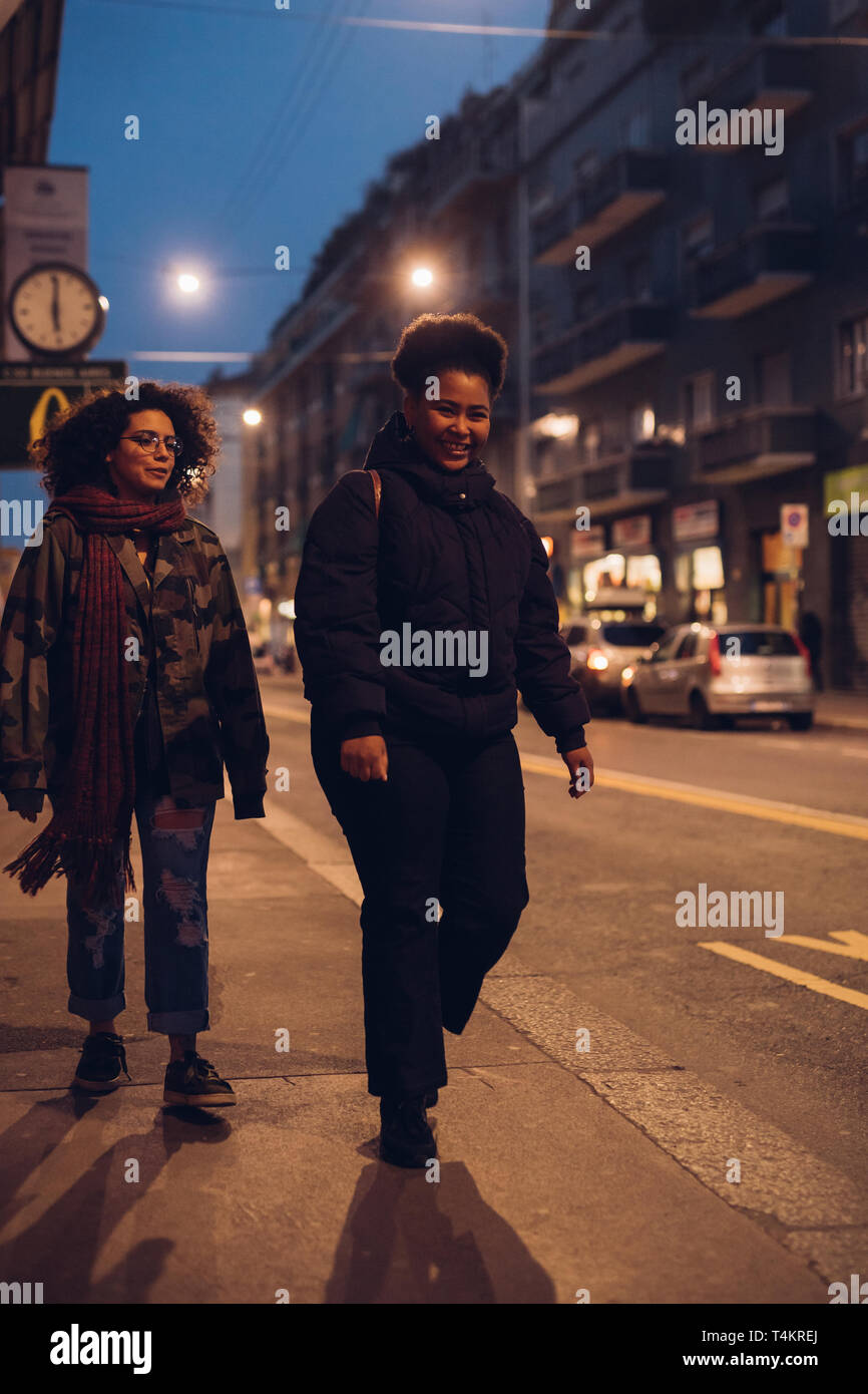 Due giovani curly ragazza camminare per la strada di sera - amicizia, comunicativo, felicità Foto Stock