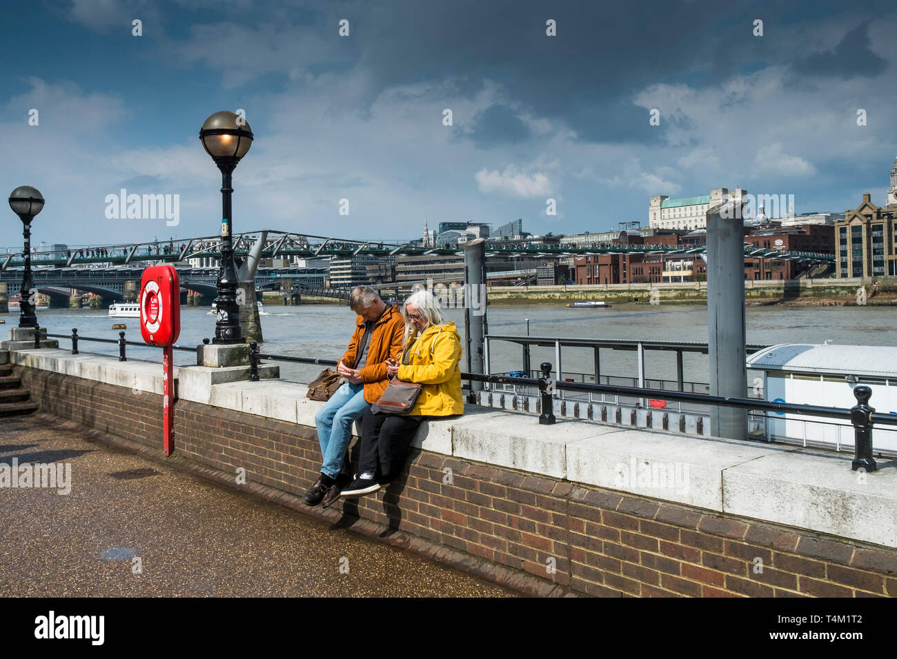 I turisti texting sui loro telefoni cellulari e seduto su una parete sulla South Bank di Londra. Foto Stock