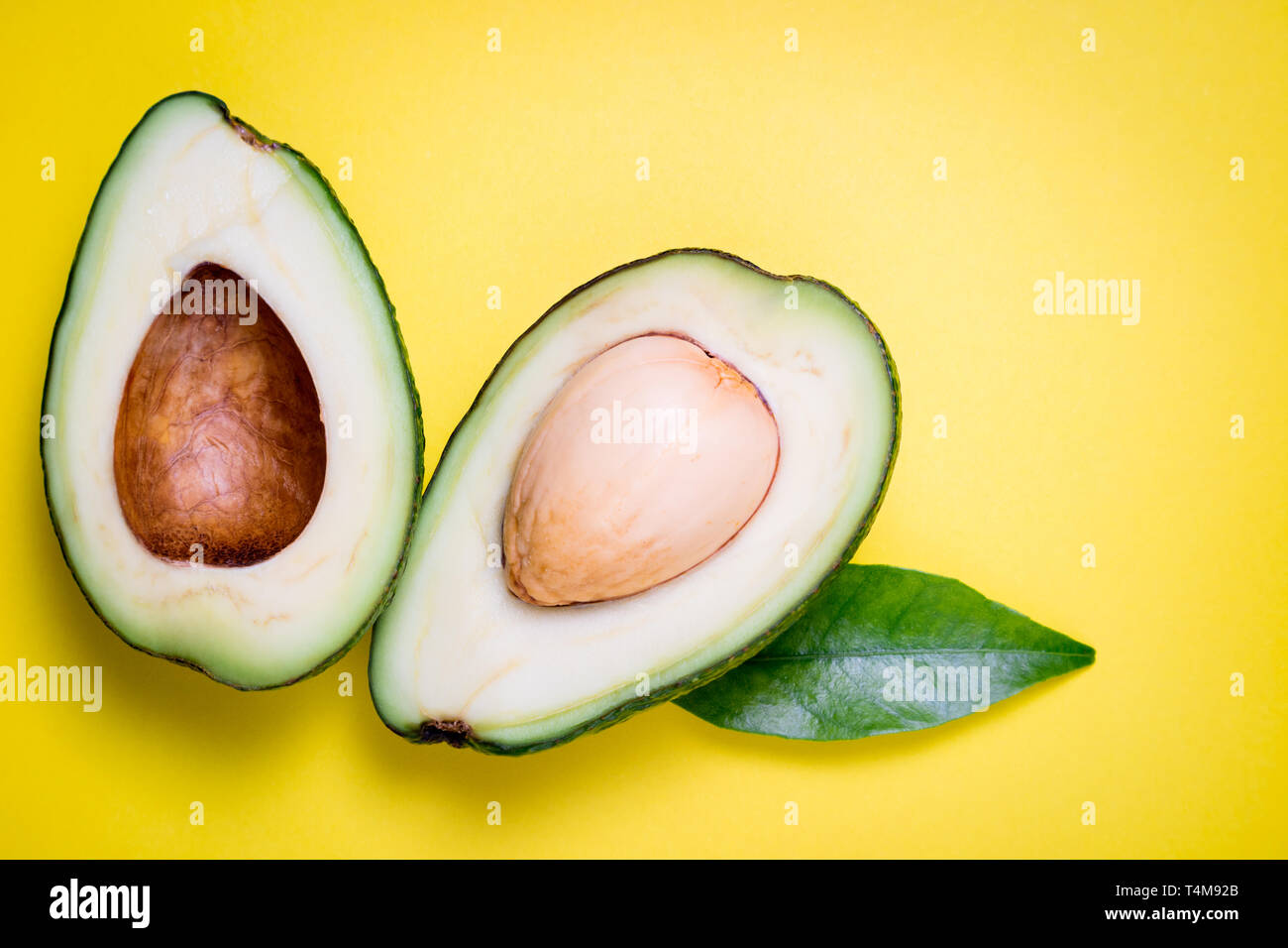Avocado su sfondo giallo. Tropical sfondo astratto con avocado e foglia. Piatto, laici vista superiore Foto Stock