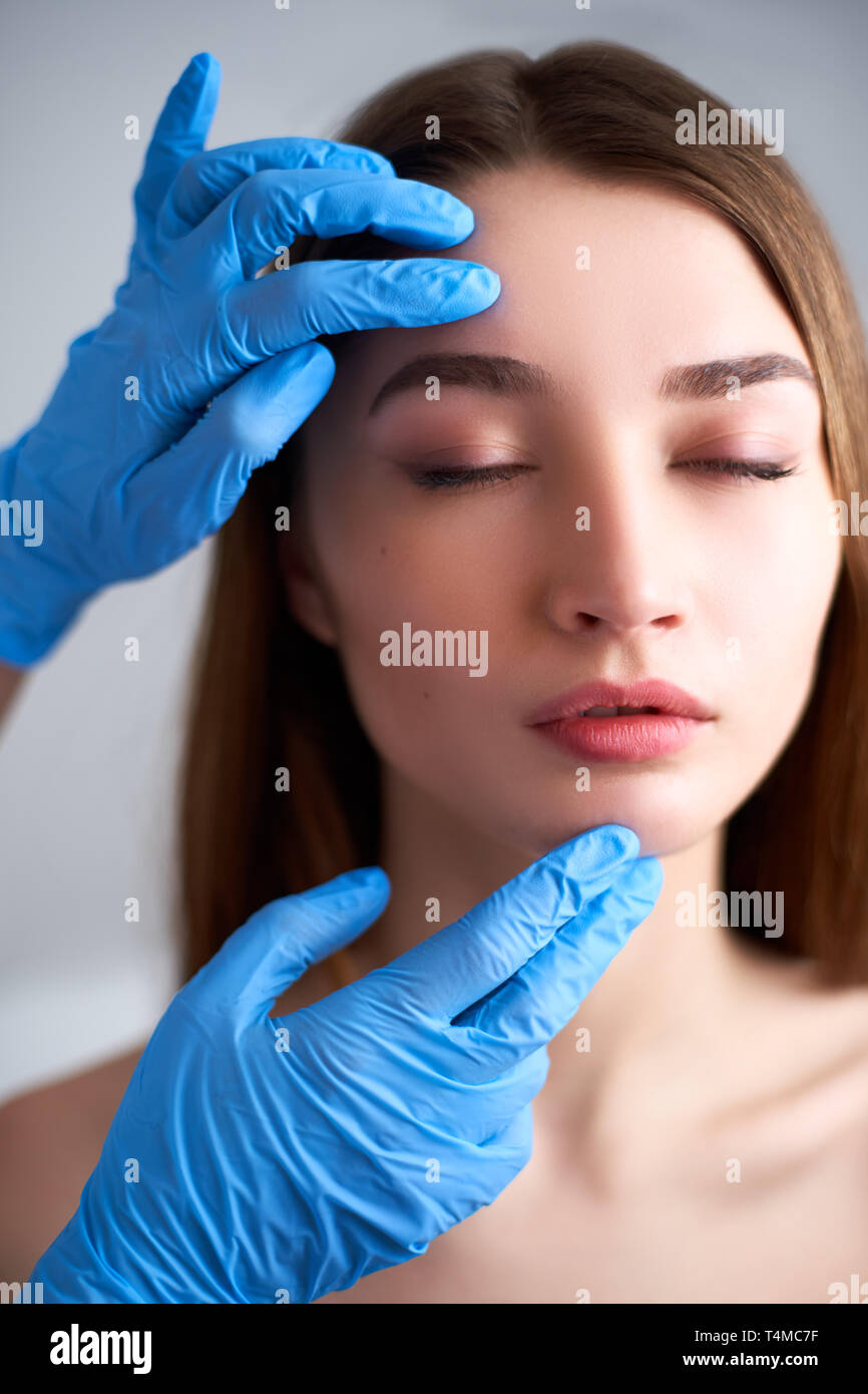 Estetista medico le mani in guanti toccando volto di donna attraente. Moda modello bionda dopo trattamento cosmetico. Cosmetologia estetica, plastica Foto Stock