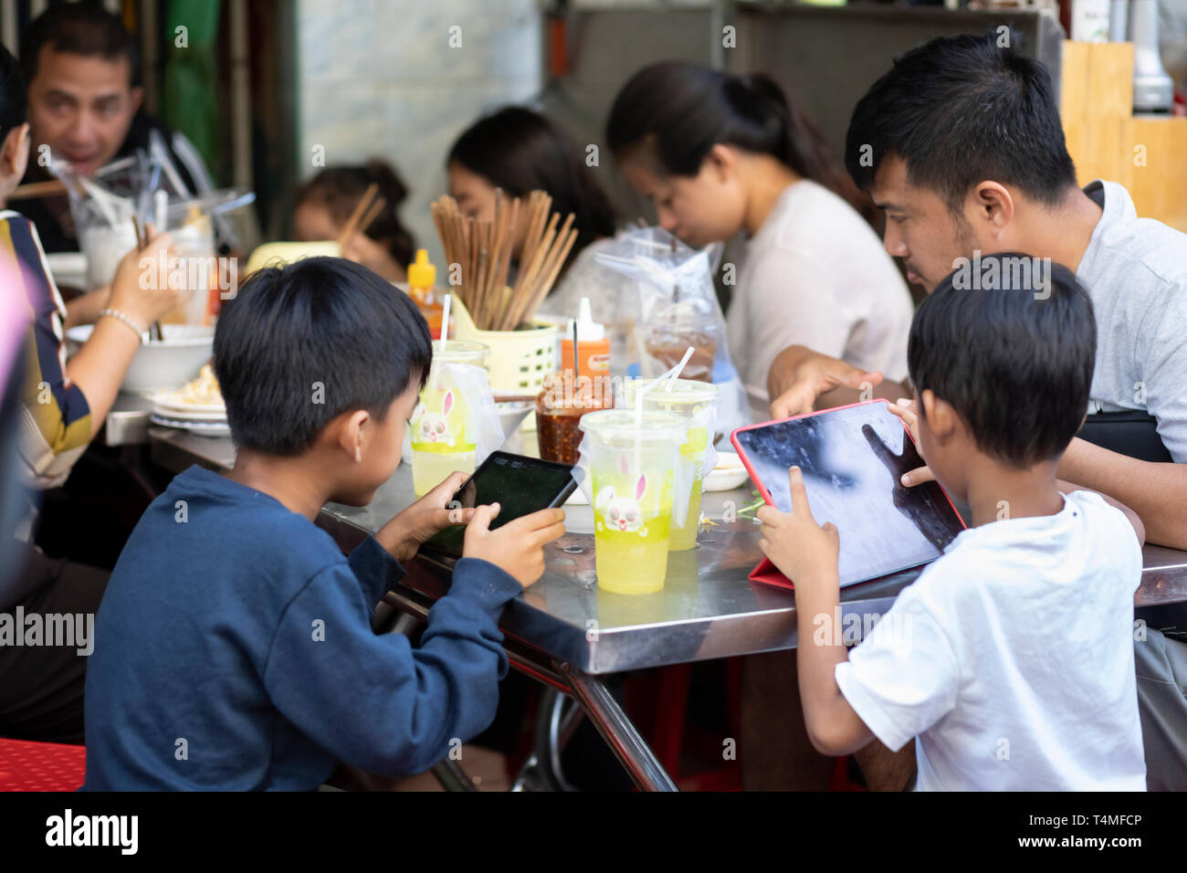 Bambini che giocano su compresse al momento dei pasti su una strada laterale vicino al Psar o mercato Russei, Phnom Penh, Cambogia, Asia sud-orientale, Asia Foto Stock