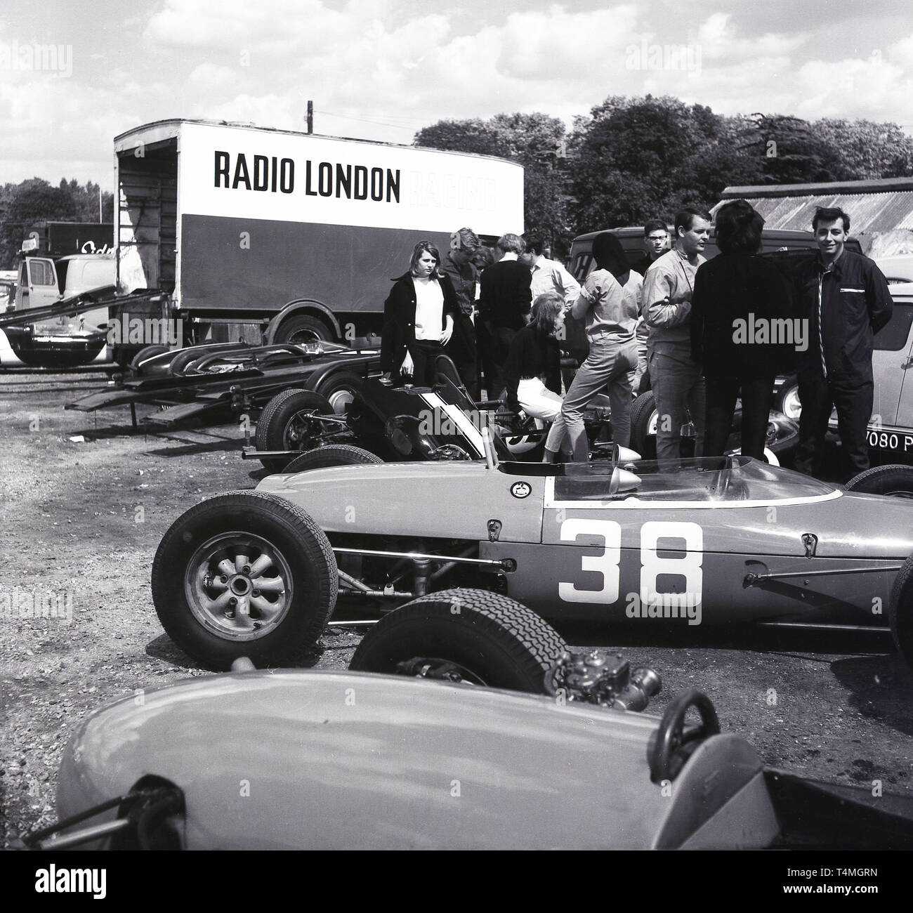 Anni sessanta, storico motor racing al Crystal Palace il circuito di gara nel sud di Londra, Londra, Inghilterra, Regno Unito. Auto parcheggiate su l'erba per camion di consegna, uno sponsorizzato da Radio Londra. Foto Stock
