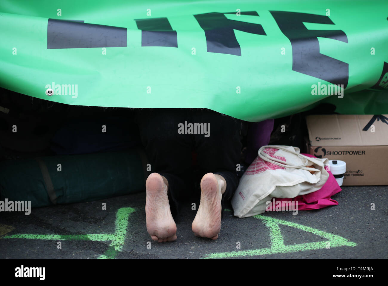 Una ribellione di estinzione demonstrator si rifugiano sotto uno del movimento poster durante una manifestazione di protesta sul ponte di Waterloo, London, come più di duecento persone sono state arrestate polizia come trattare con il cambiamento climatico in corso proteste. Foto Stock
