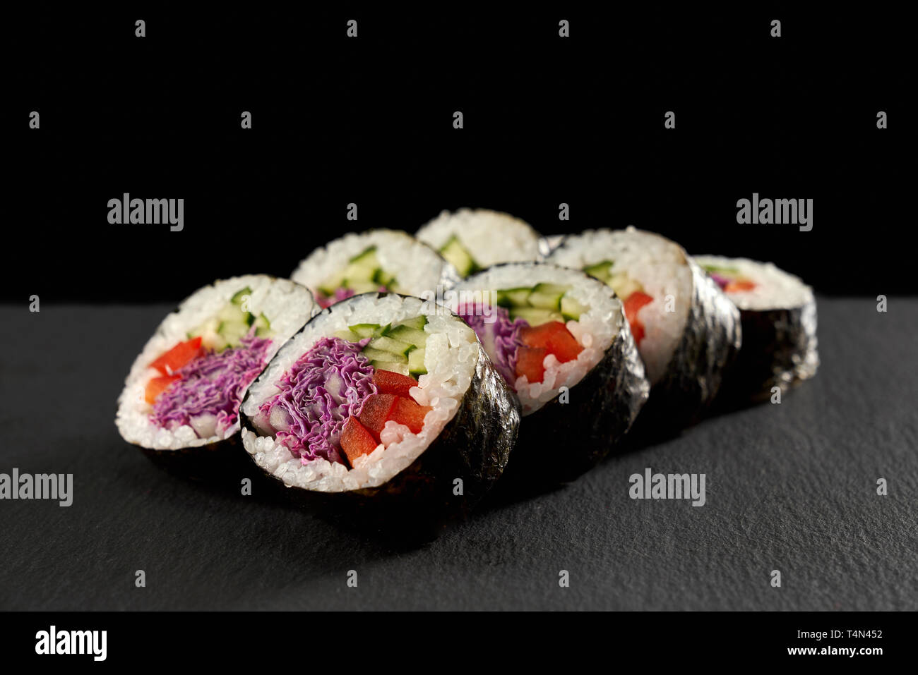 Maki vegetariani riempito con cetrioli o kappa, la paprica rossa e viola il cavolo. Veggie rotoli avvolti in nori, servita sulla pietra nera. Foto Stock