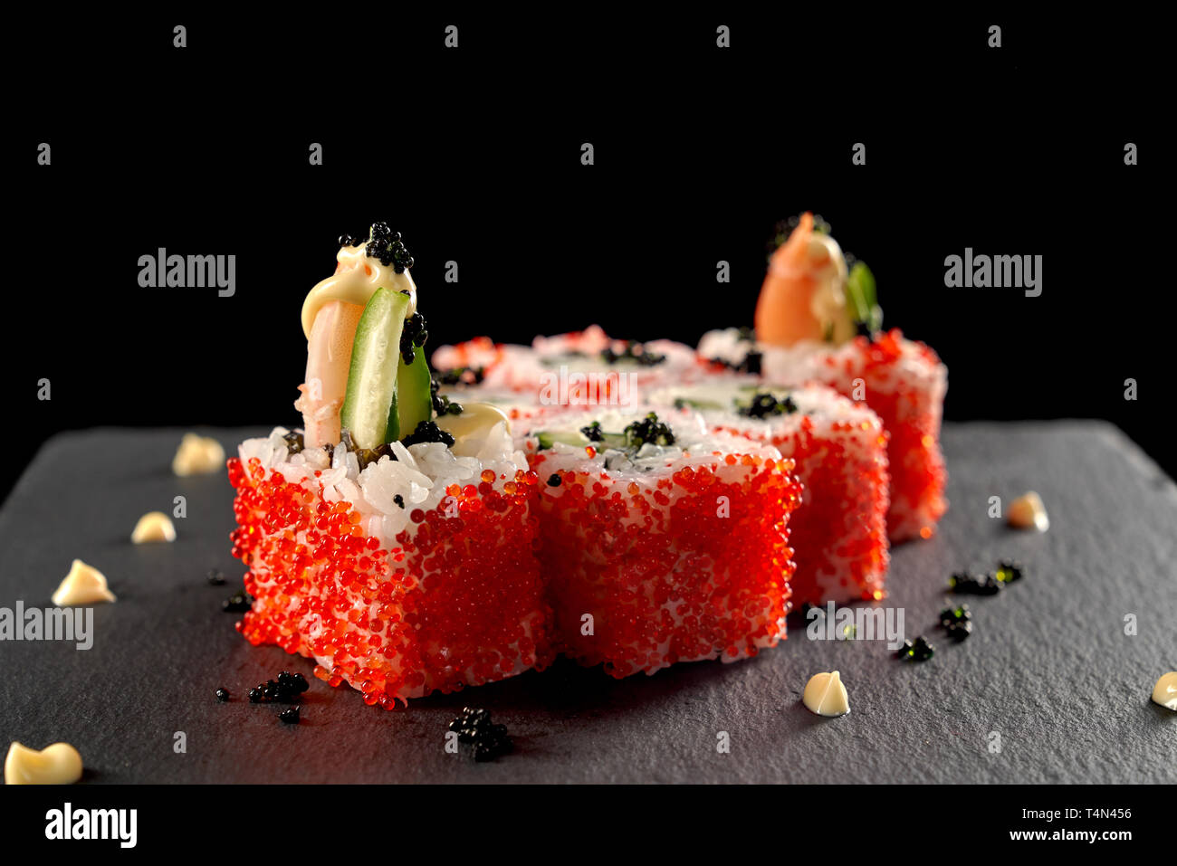 Uramaki sushi rulli rivestiti con red tobiko roe, riempito con gamberetti, cetriolo. Sushi simile a Vulcano, conditi con sugo di pomodoro e caviale nero. Servita sulla pietra nera piastra. Foto Stock