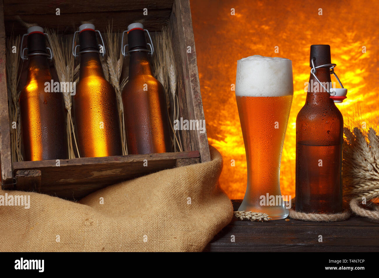 Bicchiere da birra con gabbia in legno pieno di bottiglie di birra e spighe di grano su tavola Foto Stock