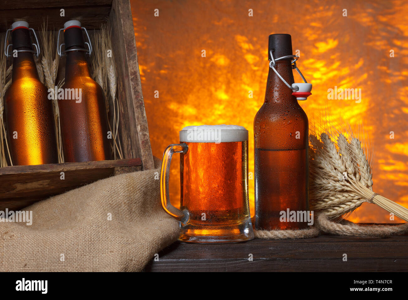 Bicchiere da birra con gabbia in legno pieno di bottiglie di birra e spighe di grano su tavola Foto Stock