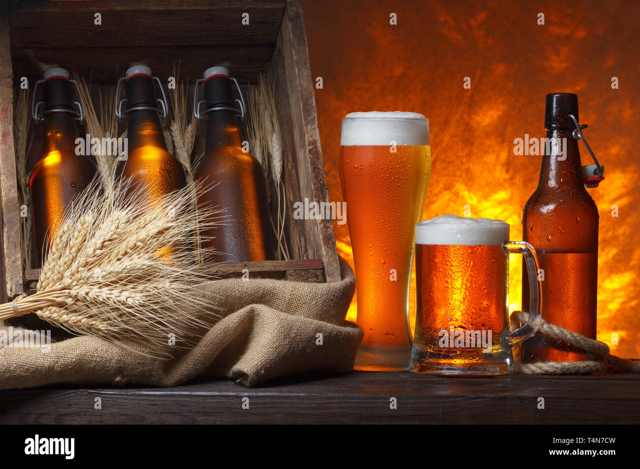 Bicchieri da birra con gabbia in legno pieno di bottiglie di birra e spighe di grano su tavola Foto Stock