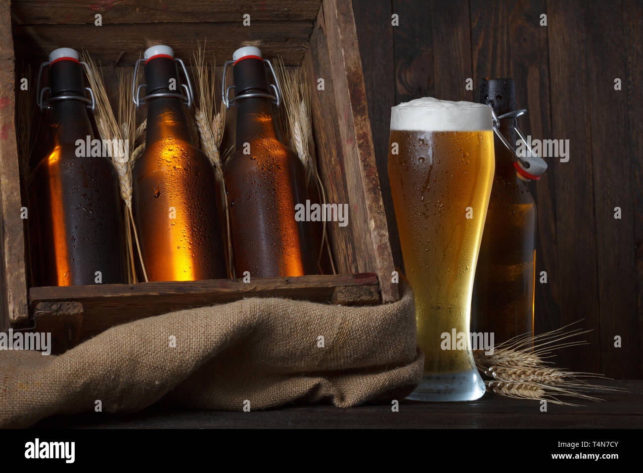 Bicchiere da birra con gabbia in legno pieno di bottiglie di birra e spighe di grano Foto Stock