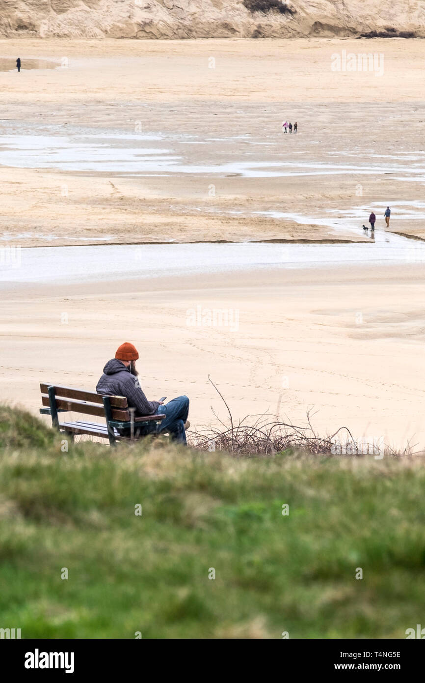 Un uomo seduto da solo su una panchina affacciata Crantock Beach in Newquay in Cornovaglia. Foto Stock