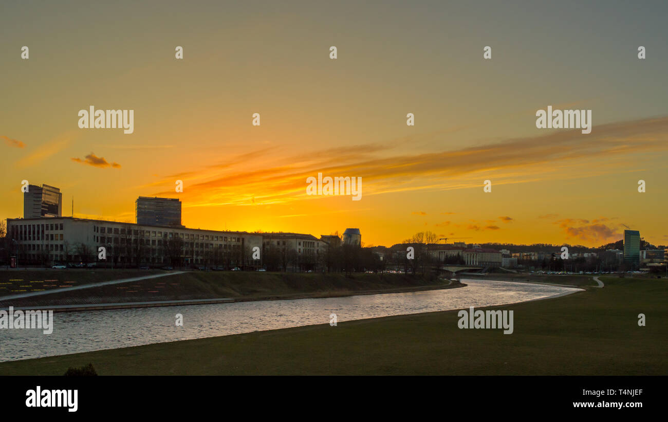 Un bel colore arancione tramonto su un fiume e gli edifici sagome in Vilnius city centre Foto Stock