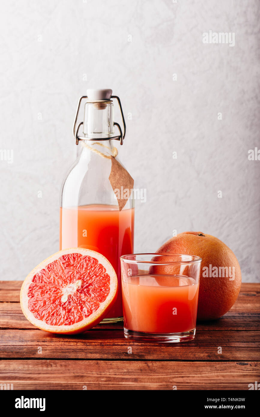 Bottiglia di succo di pompelmo con vetro e frutta su una superficie di legno Foto Stock