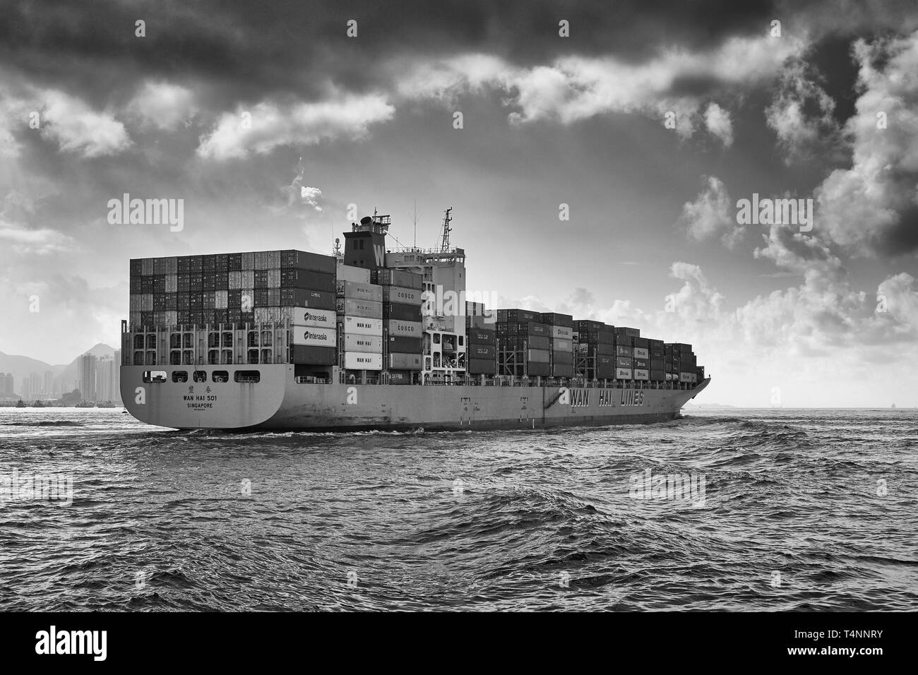 Foto in bianco e nero Moody di Una nave container WAN hai LINES, WAN hai 501, che entra nell'affollato canale East Lamma mentre lascia Hong Kong Foto Stock