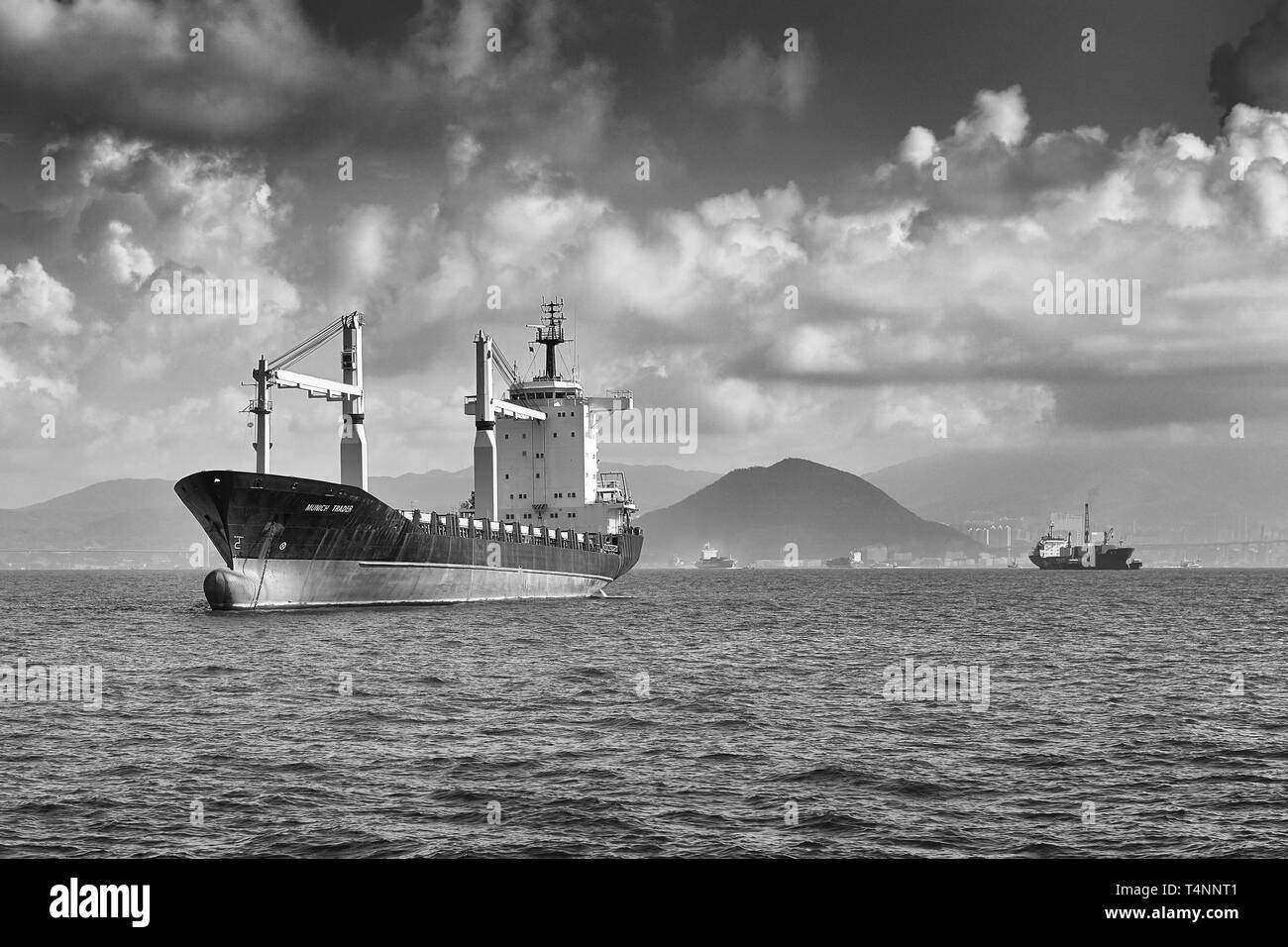Foto Moody in bianco e nero della nave cargo/container, COMMERCIANTE DI MONACO, in-Ballast e ancorata a ovest di Victoria Harbour, Hong Kong. Foto Stock
