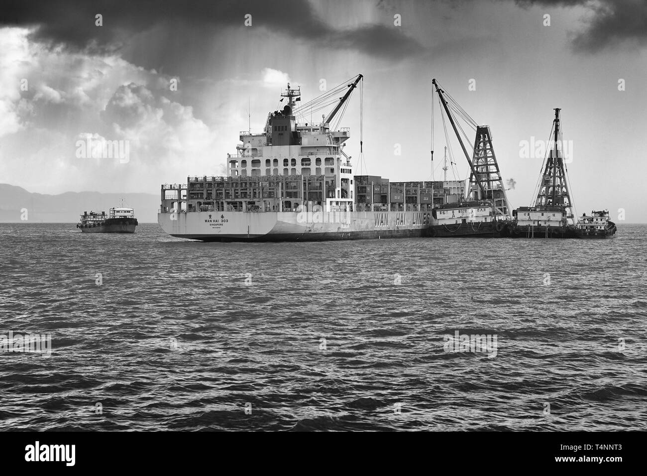 Foto Moody in bianco e nero della nave container WAN hai LINES, WAN hai 303, scarico di container in Un'operazione Mid-Stream, Hong Kong. Foto Stock