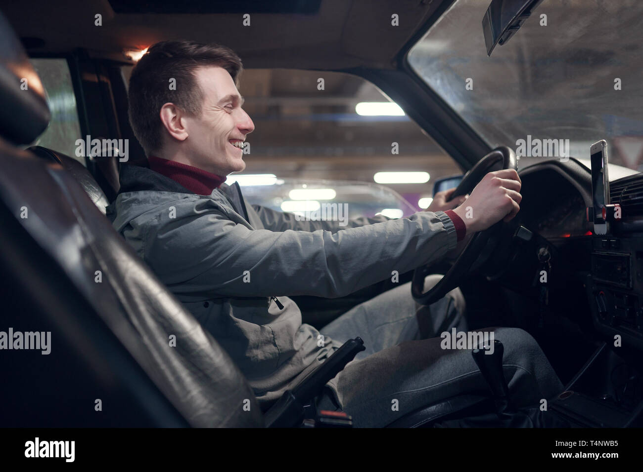 Foto dal lato del giovane uomo sorridente seduto in auto. Foto Stock