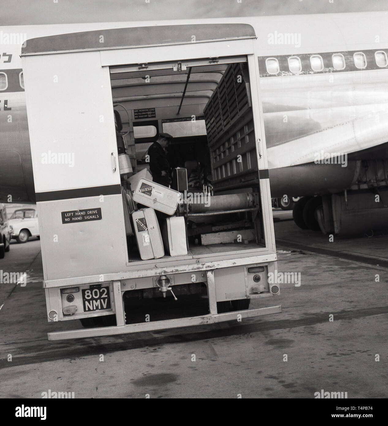 Anni sessanta, storiche, l'aeroporto di Heathrow di Londra, Inghilterra, Regno Unito. La figura mostra la parte posteriore aperta di a. " Guida a sinistra' van con interno il nastro trasportatore parcheggiato a fianco di un aereo sulla pista di prendere i bagagli dei passeggeri dal piano. Foto Stock